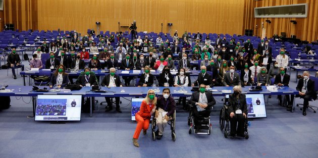 A large group of people with face masks posing in the plenary room at the UN Offices in Vienna